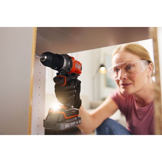 A woman builds flat-packed furniture using the BLACK+DECKER® POWERCONNECT™ 18V Cordless Drill Driver.