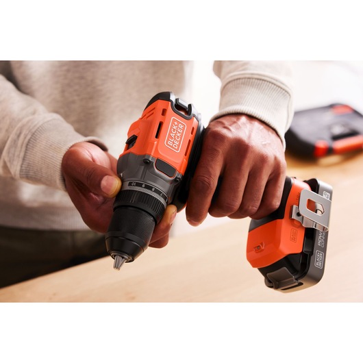 Person holding a BLACK+DECKER cordless drill and battery, preparing for use on a wooden surface.