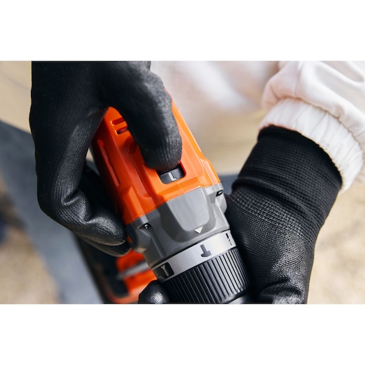Photo of BLACK+DECKER BCD383D1 cordless drill in use, close-up on mode selector switch and gloved hands.
