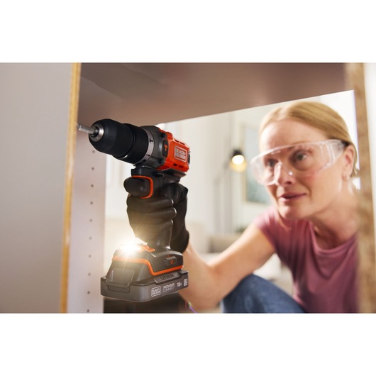 A woman builds flat-packed furniture using the BLACK+DECKER® POWERCONNECT™ 18V Cordless Hammer Drill.