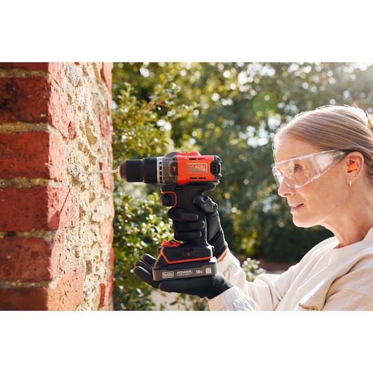A woman drills into brickwork using the BLACK+DECKER® POWERCONNECT™ 18V Cordless Hammer Drill.