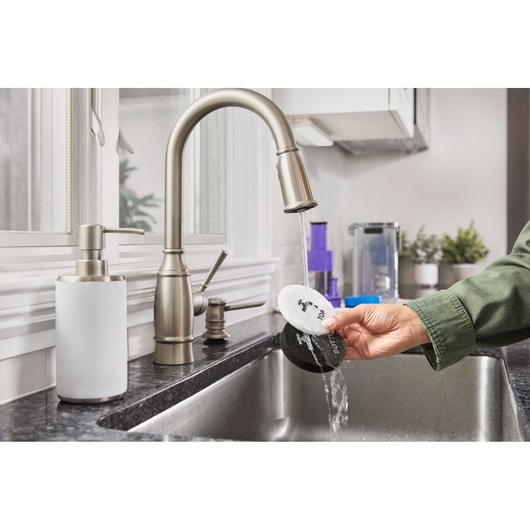 Photo of a hand rinsing BLACKDECKER BHFEA640WP cleaning pads under a kitchen faucet in a modern sink.