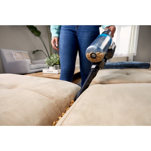 Woman using the crevice tool with the POWERSERIES Extreme MAX cordless stick vac to clean crumbs out of couch cushions