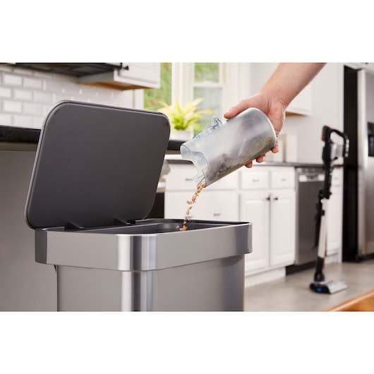 Man dumping debris out of the dustbowl of the POWERSERIES Extreme MAX stick vac into a trashcan