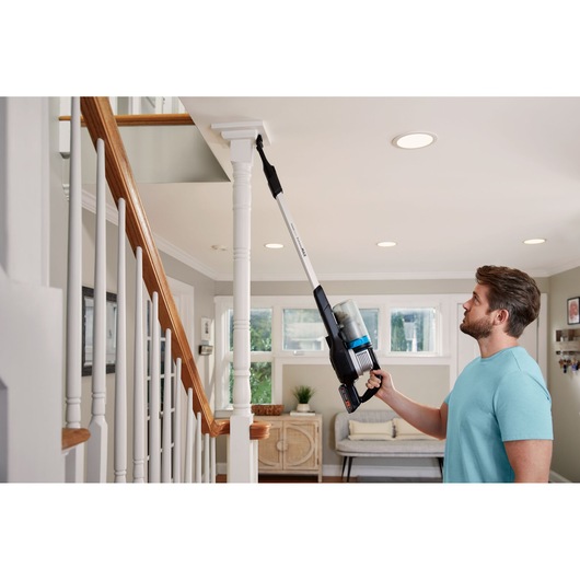BLACKDECKER BHFEB520D1 vacuum cleaner with long reach used for cleaning above a stair post in a living room.