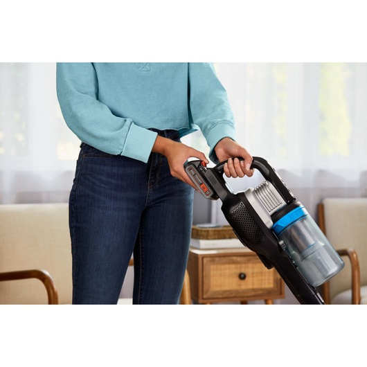 Photo of person holding BLACKDECKER cordless stick vacuum BHFEB520D1 with blue dustbin in living room.