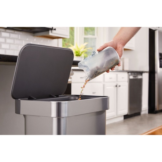 Photo of BLACKDECKER BHFEB520D1 dirt canister being emptied into kitchen trash bin.
