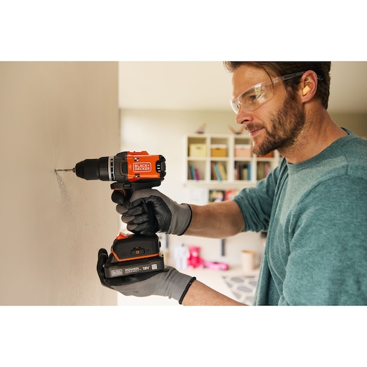 Photo of person using BLACK+DECKER BLD682D1 cordless drill on interior wall, wearing gloves.