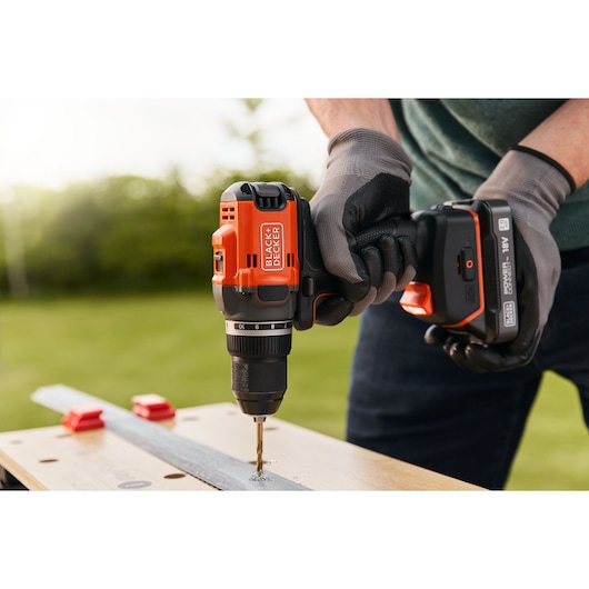 BLACK+DECKER BLD682D1 cordless drill being used to drill into metal on a wooden workbench, outdoor setting.
