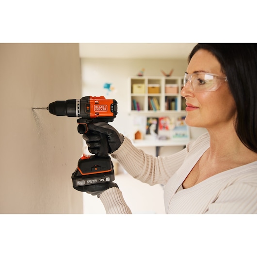 A woman drills into an interior wall using the BLACK+DECKER® 18V POWERCONNECT™ Brushless Hammer Drill.