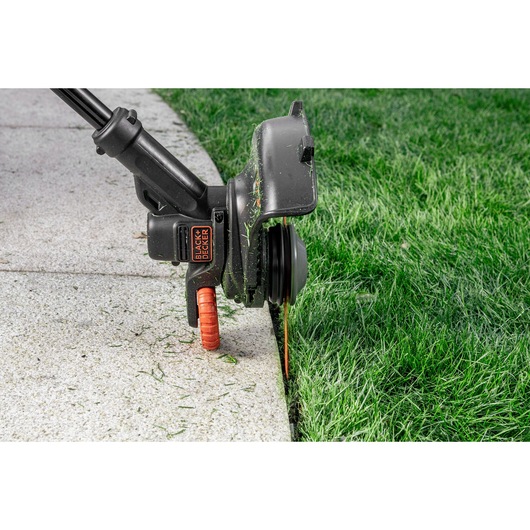 BLACK+DECKER BZOS2B1 grass trimmer head cutting lawn edge next to concrete walkway, close-up.