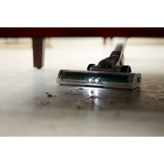 Close-up of dirt under a couch being vacuumed by the BLACK+DECKER® reviva™ 18V POWERCONNECT™ Cordless Stick Vacuum.